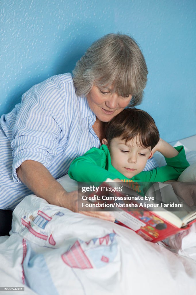 Grandmother and grandson reading book in bed