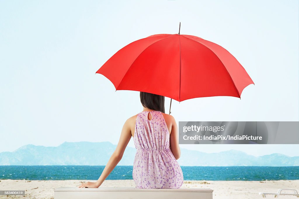 Woman sitting in front of sea with umbrella