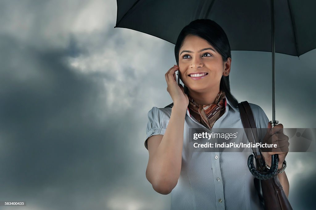 Woman with umbrella talking on mobile phone