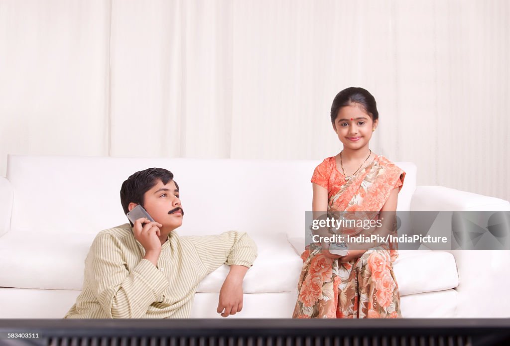 Boy talking on mobile phone while girl watches tv