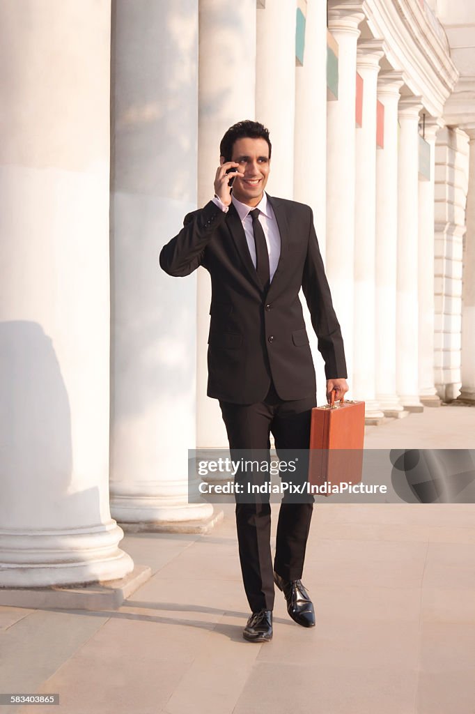 Businessman with suitcase talking on a mobile phone  , INDIA , DELHI