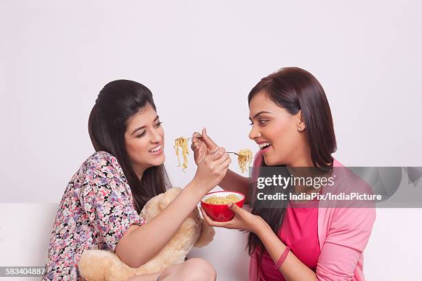 two young women eating noodles - maggi noodles stock pictures, royalty-free photos & images