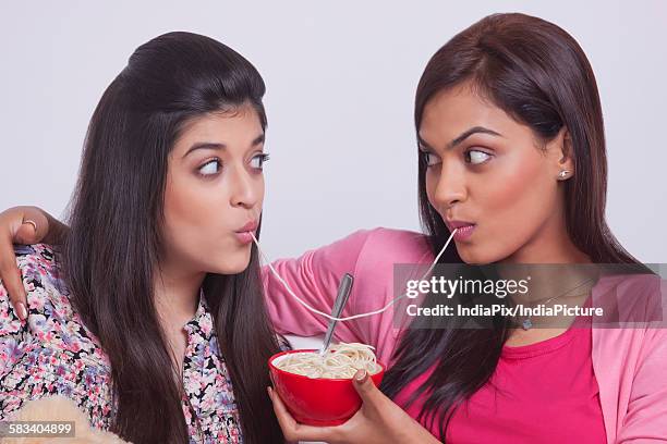 two young women eating noodles - maggi noodles stock pictures, royalty-free photos & images