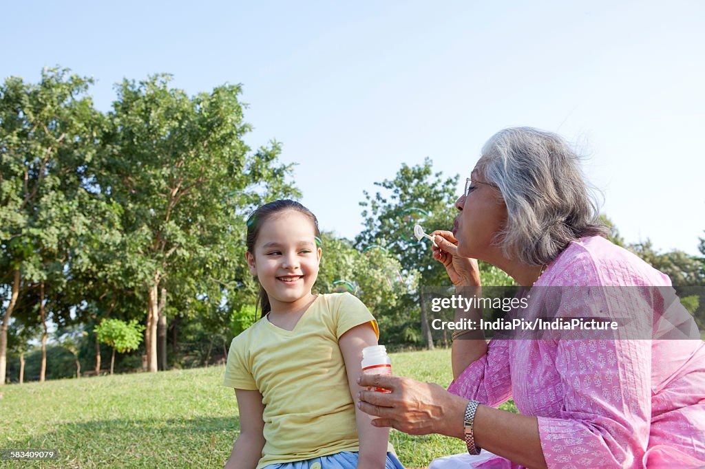 Grandmother blowing bubbles at granddaughter