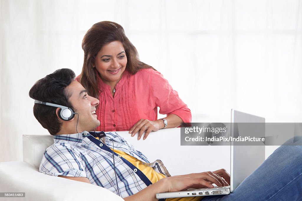 Young man listening to music while mother looks at laptop