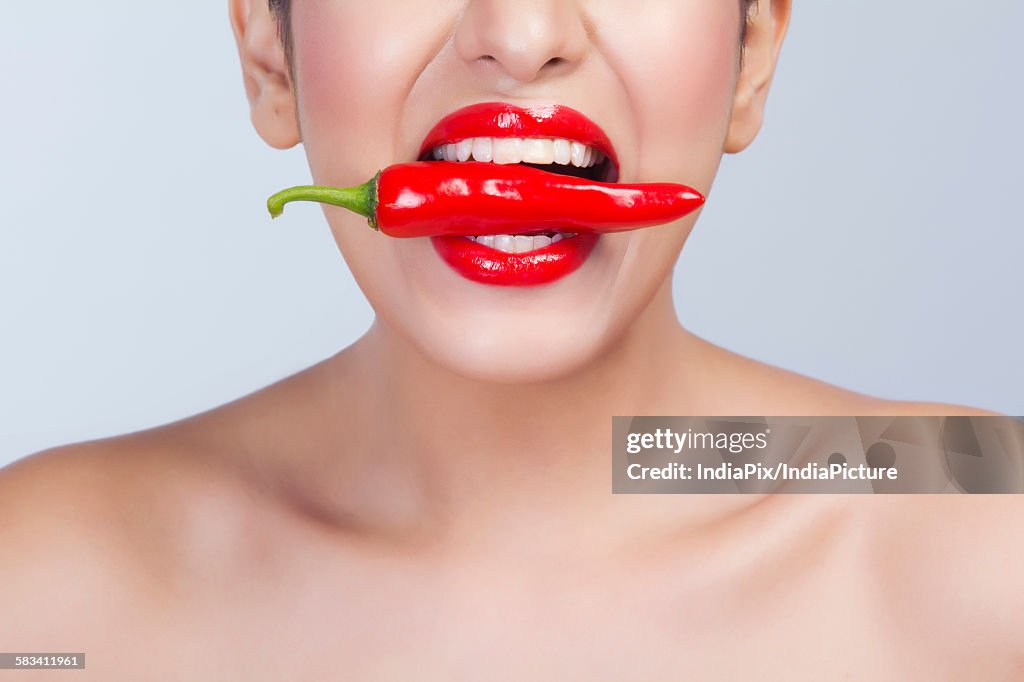 Woman with red pepper between her teeth