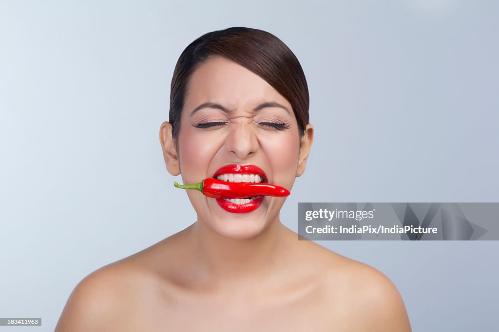 Woman with red pepper between her teeth