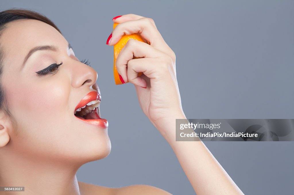 Woman squeezing juice from orange into her mouth