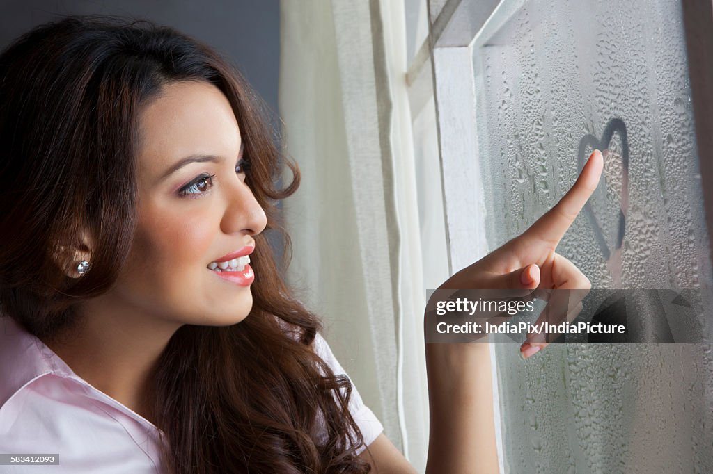 Woman drawing heart on window