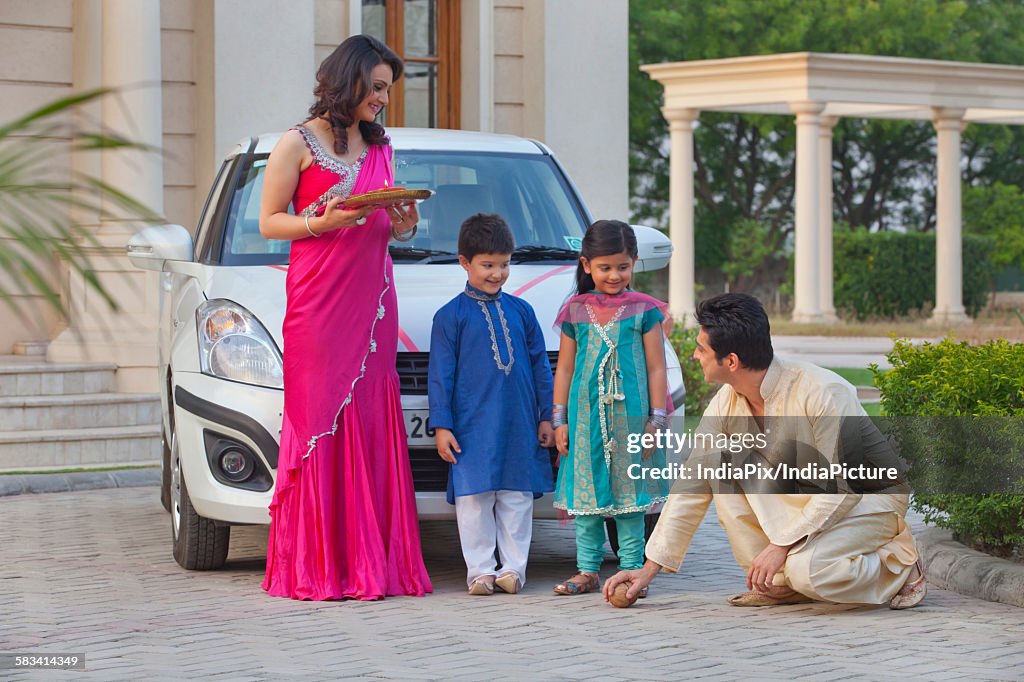 Man breaking coconut on ground as family watches on