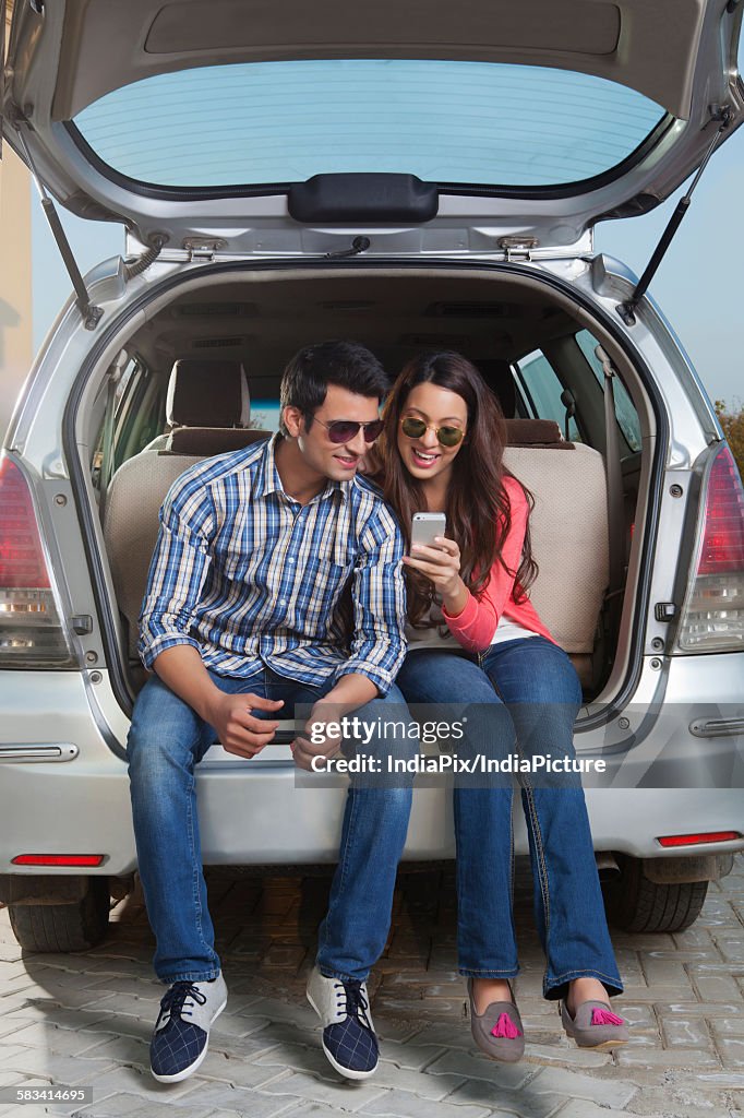 Young man and young woman sitting in the trunk of a car