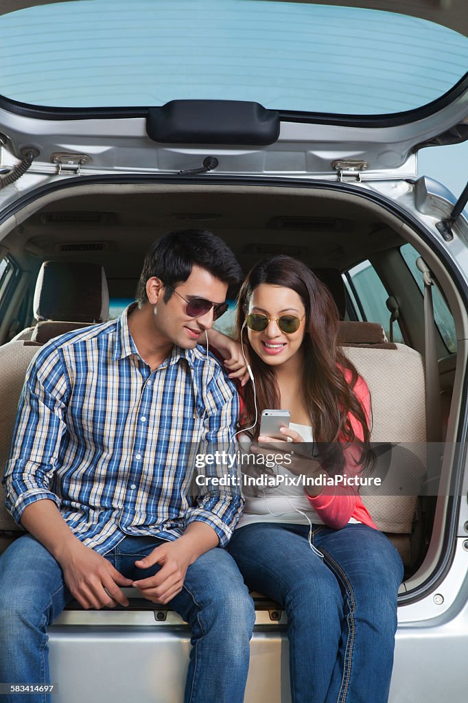 Young man and young woman sitting in the trunk of a car