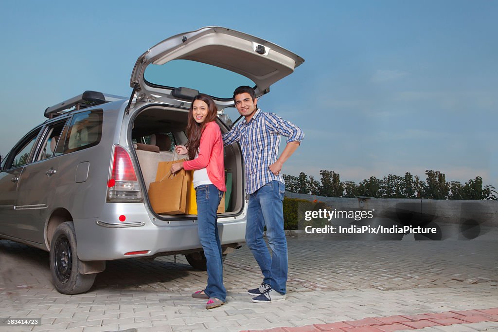 Young man and young woman keeping bags in trunk of car