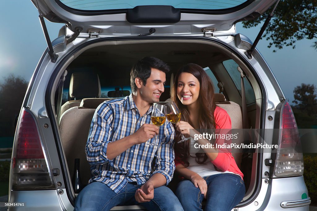 Young man and young woman sitting in the trunk of a car