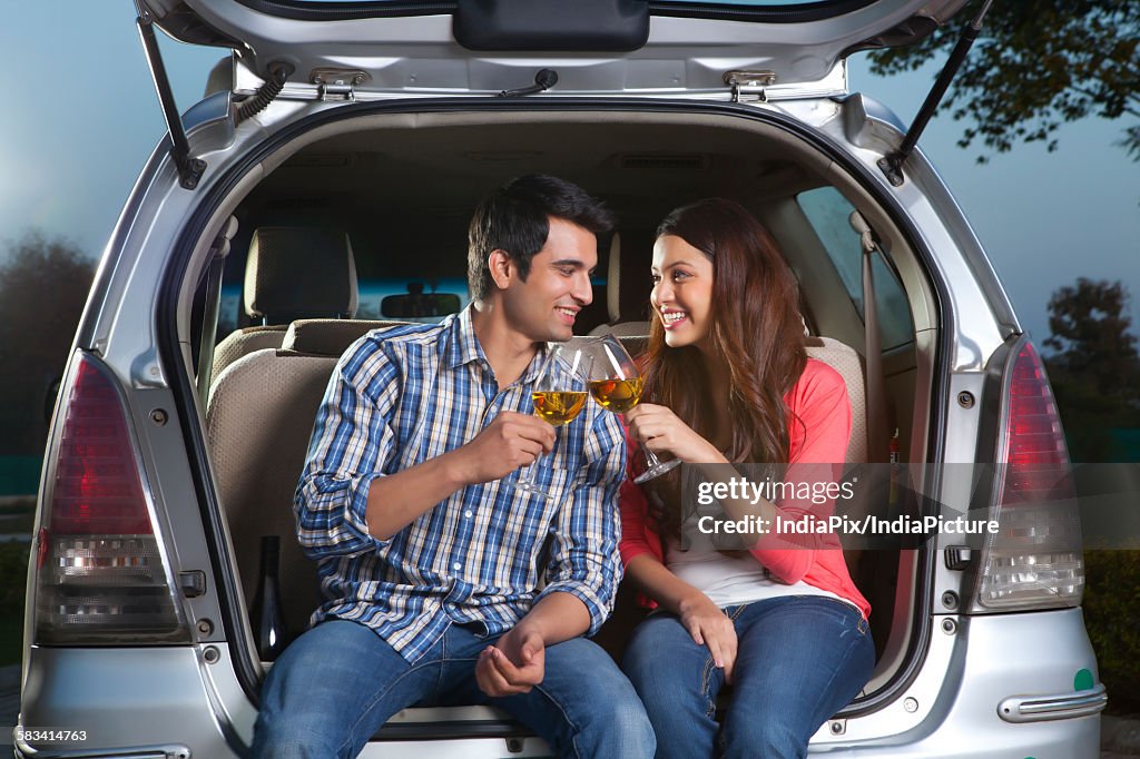 Young man and young woman sitting in the trunk of a car