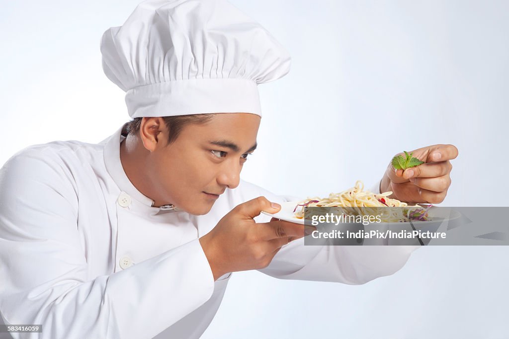 Chef placing leaf on plate of noodles