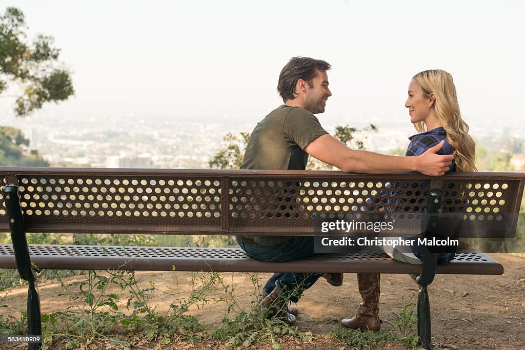 Young couple joke on park bench overlooking city