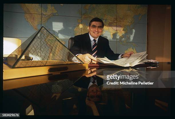 Jean-Louis Beffa sits at his office in front of a world map and beside a scale model of the Louvre pyramid.