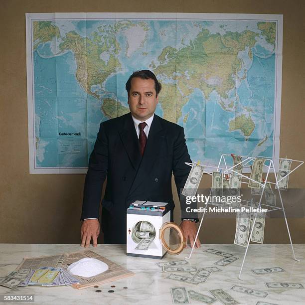 French writer Paul Lou Sulitzer stands before a world map, with dollar bills hanging on a dryer, others displayed on a table, a small washing-machine...