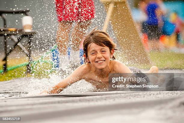 young boy splashing down on a slip n slide - wasserleiche stock-fotos und bilder