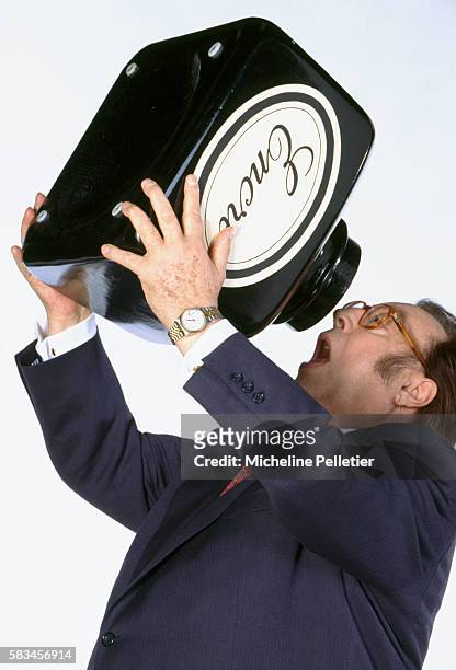 Popular Belgian comedian Raymond Devos pretends to drink ink from an oversized ink bottle. Devos is author of the 1996 book, Un Jour Sans Moi.