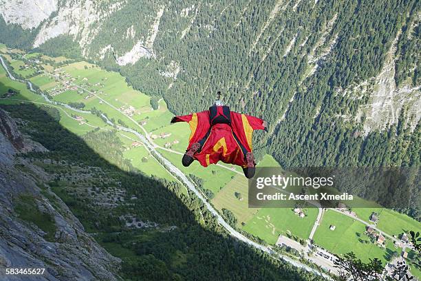 wingsuit flier in airborne descent towards valley - wing suit stock pictures, royalty-free photos & images