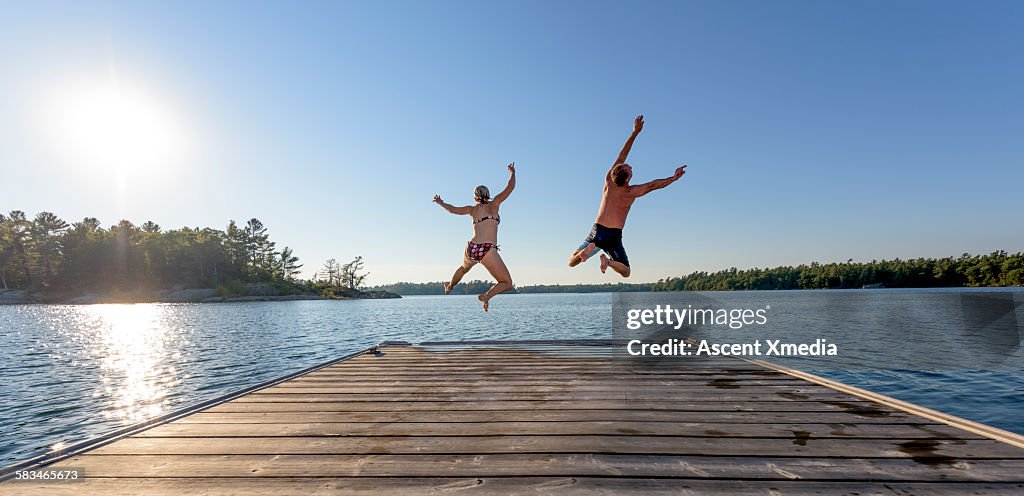 Man and woman jump off boat dock, expressively