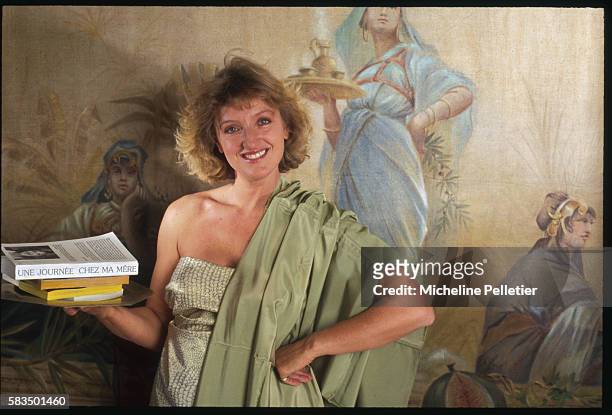 Swathed in Grecian robes, Charlotte de Turckheim poses with her book, Une Journee Chez Ma Mere, mirroring the motif of the mural behind her.
