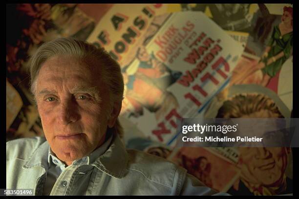 American actor, Kirk Douglas, relaxes at home, in front of a wall-sized collage of his film posters.