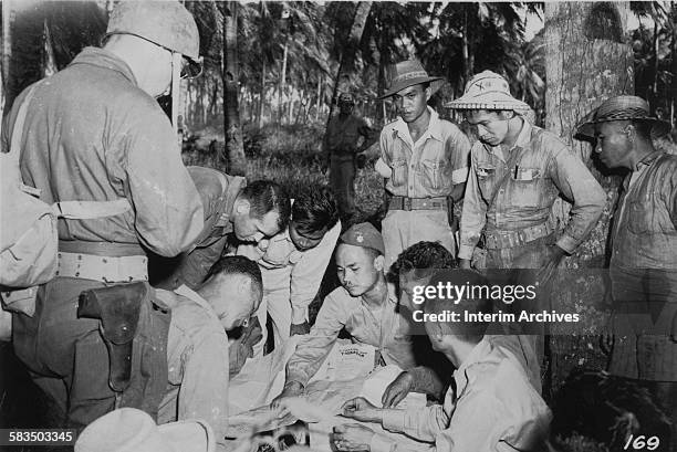 View of Panay guerilla leaders huddled around a map while in conference with American Division G-2 soldiers, Panay, Philippines, 1940s.