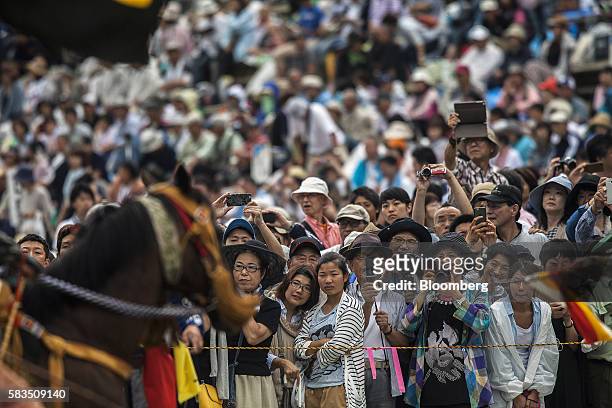 Spectators take photographs of competing samurai horseman in the Kachu Keiba race during the Soma Nomaoi festival at Hibarigahara field in...