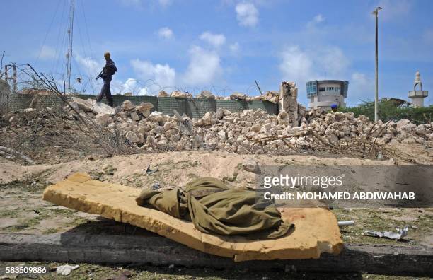 Somali soldiers passes the partially-crumbled perimeter wall as the body of a collegue lies nearby following twin car bombings outside the UN's...