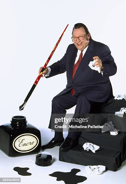 Popular Belgian comedian Raymond Devos holds an oversized fountain pen next to a large ink bottle. Devos is author of the 1996 book, Un Jour Sans Moi.