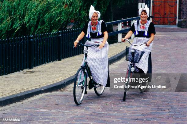 two dutch women ride bicycles on street - volendam photos et images de collection