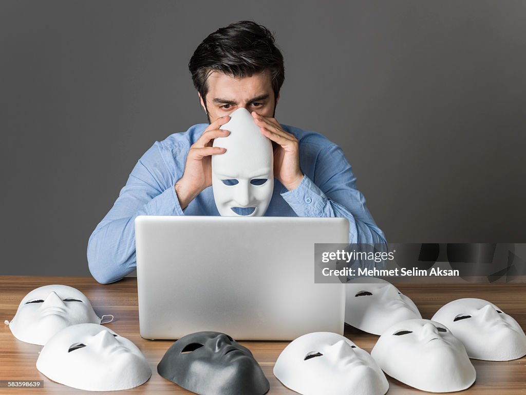 Young man holding mask in front of computer