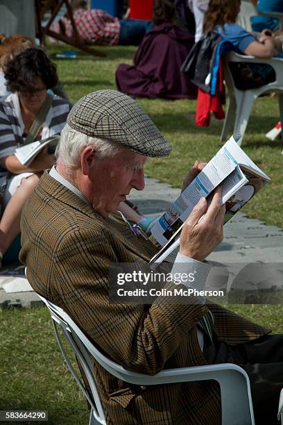 An elderly man wearing traditional Tweed jacket and cap reading the official programme on the opening weekend of the the Edinburgh International Book...