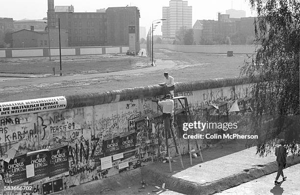 Two anti-GDR protesters sitting on top of a section of the Berlin Wall between the Brandenburg Gate and Potsdamer Platz in the centre of the city are...