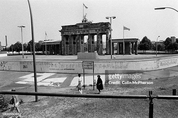 People walking past a section of the Berlin Wall at the Brandenburg Gate, seen from the western side of the divide. The Berlin Wall was a barrier...