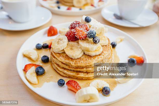 stack of pancakes with maple syrup, banana, strawberry and blueberry on the plate - toetje stockfoto's en -beelden