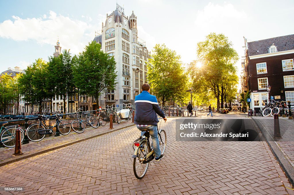Man on bike riding on the streets of Amsterdam at sunset, Netherlands