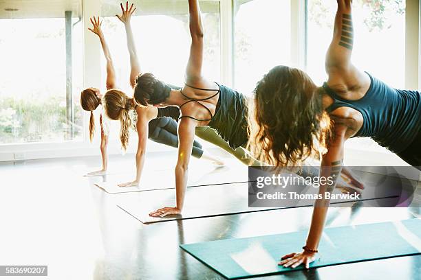 Women practicing yoga in side plank pose in class