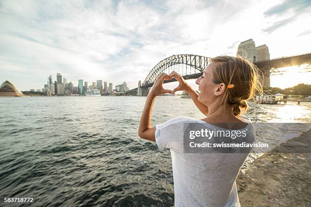 young woman in sydney harbour makes heart shape finger frame - sydney harbour people stock pictures, royalty-free photos & images