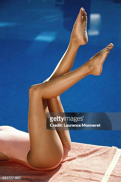 young woman lying beside swimming pool, legs in air, section view - piernas de mujer fotografías e imágenes de stock