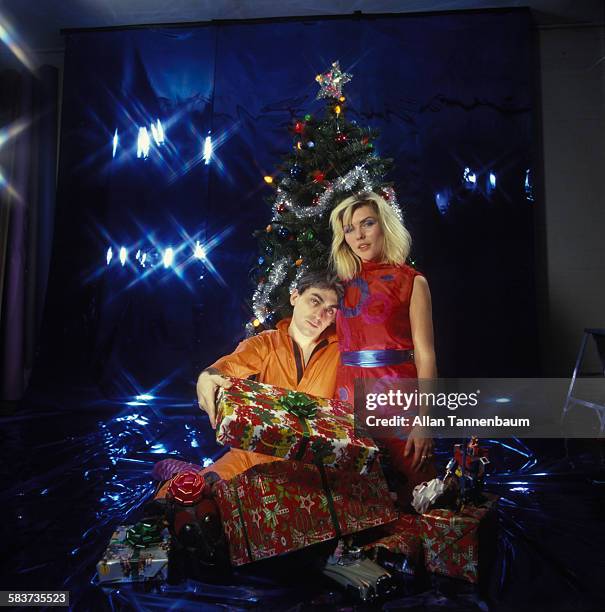 Studio portrait of American musicians Chris Stein and Debbie Harry, both of the group Blondie, as they pose in front of a Christmas tree and offer...