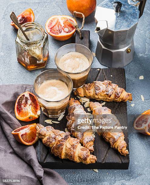 traditional italian style home breakfast. latte in glasses, almond croissants and red bloody sicilian oranges over concrete textured table - moka pot stockfoto's en -beelden