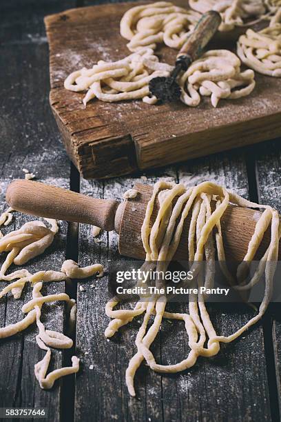 fresh homemade pici pasta on wood chopping board over old wooden table with flour and rolling-pin. dark rustic style. with retro filter effect - wood effect stock-fotos und bilder