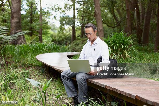 man sitting on walkway using laptop computer - laptoptasche stock-fotos und bilder