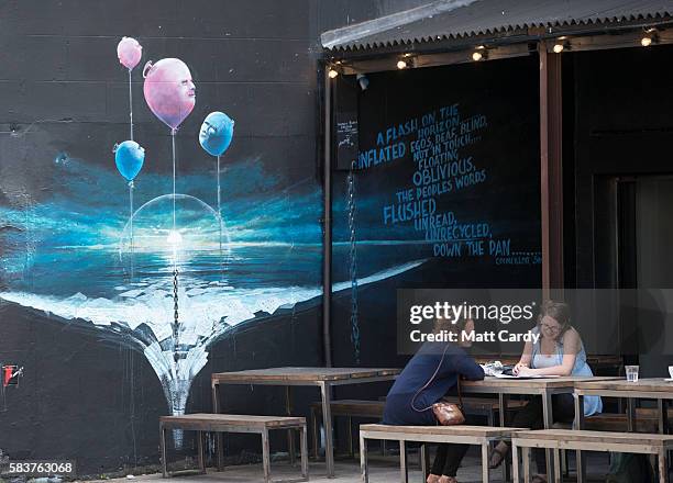 People sit in a cafe beneath artwork produced as part of the 2016 Upfest on July 27, 2016 in Bristol, England. The annual event, which this year...