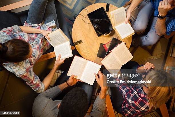 diverse group of friends discussing a book in library. - georganiseerde groepen stockfoto's en -beelden