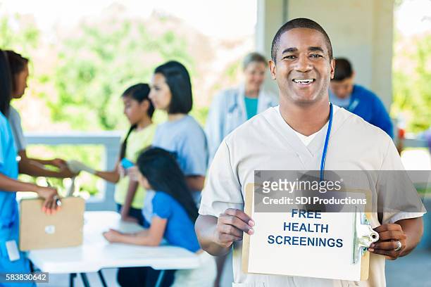 handsome doctor holding a ""free health screenings"" sign - film and television screening stock pictures, royalty-free photos & images
